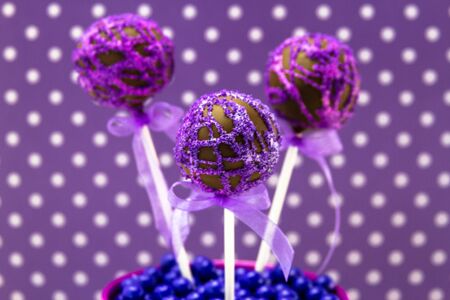 Chocolate cake pops with purple swirl glitter sugar decorations against purple polka dot backgroundの写真素材
