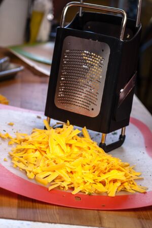 Grated yellow cheddar cheese sitting on kitchen work station next to large cheese graterの写真素材