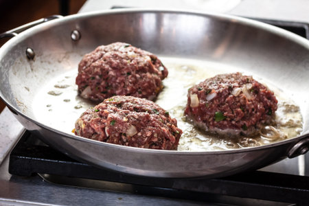 Raw hamburgers cooking in hot stainless steel pan on stove