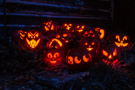Carved Halloween pumpkins lit with candles sitting on leaves in front of old barn lit with purple lightの写真素材