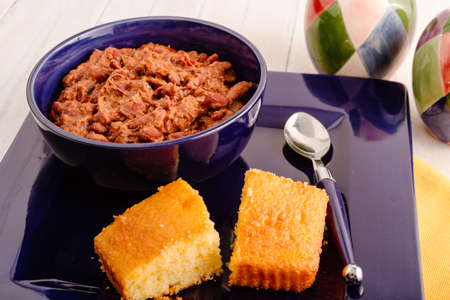 Bowl of elk meat chili sitting in blue bowl and plate with cornbreadの写真素材