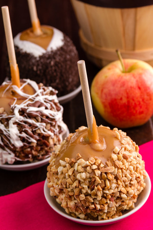 Group of caramel covered apples decorated with nuts and chocolate sitting on bright pink napkinの写真素材