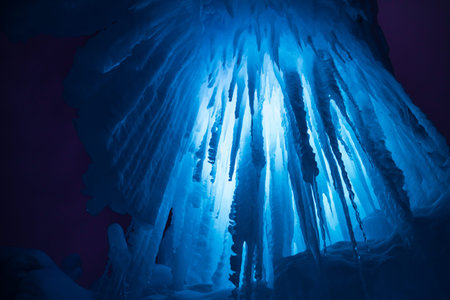 Abstract ice and icicles formations on cold winter night covered in snow and blue colored lights