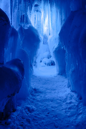 Abstract ice and icicles formations forming ice caves on cold winter day covered in snow and blue...
