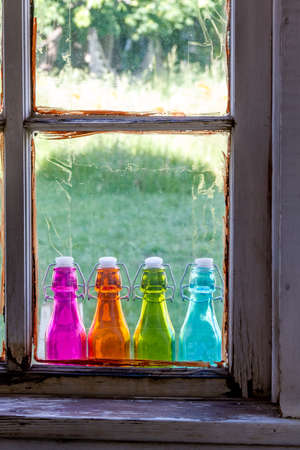 Looking through old window at colored vintage bottles sitting on wooden window sillの写真素材