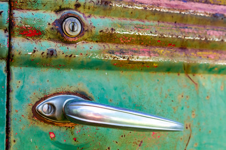 Close up of door handle and lock on colorful rusting door of abandoned green pick up truck in fieldの写真素材