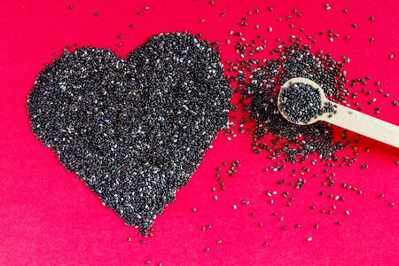 Black chia seeds arranged in heart shape with small spoon on red backgroundの写真素材
