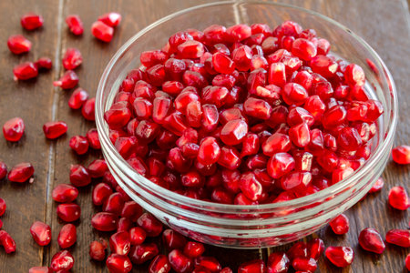 Fresh organic pomegranate seeds in glass bowl on dark wooden tableの写真素材
