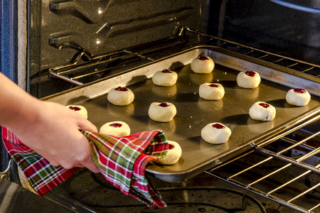 Pan of raspberry thumbprint cookies sitting on baking sheet being placed in oven to bakeの写真素材