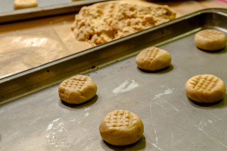 Rows of peanut butter cookie dough balls on baking pans sitting on counter waiting to be baked