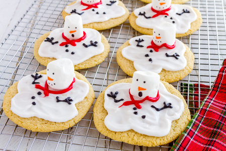 Melting snowman sugar cookies sitting on wire baking rack with colorful holiday napkin
