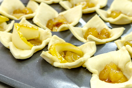 Close up of pear brown sugar compote hors doeuvres sitting in puff pastry cups on baking pan waiting to go into ovenの写真素材