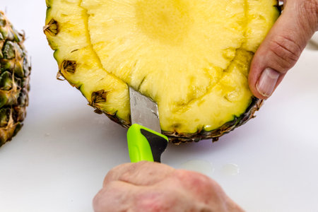 Close up of female hands cutting out the core of fresh whole pineapple sitting on cutting boardの写真素材