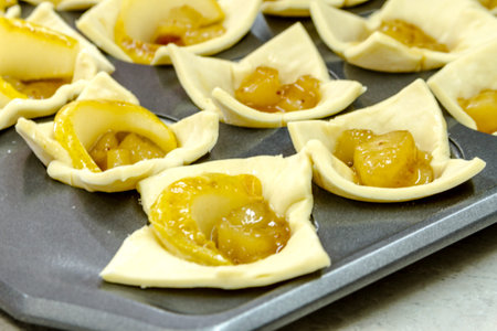 Close up of pear brown sugar compote hors doeuvres sitting in puff pastry cups on baking pan waiting to go into ovenの写真素材