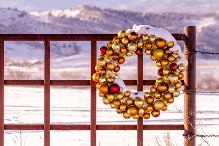 Gold and brown Christmas ornament wreath covered with freshly fallen snow sitting on entrance to mountain ranch fenceの写真素材