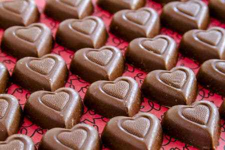 Rows of chocolate heart shaped candies filled with fudge sitting on red background with black text spelling loveの写真素材