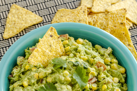Close up of homemade chunky guacamole with fresh corn in bright blue bowl and yellow corn tortilla chipsの写真素材
