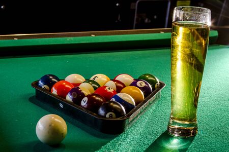Colorful billiard balls in triangle rack with cue ball sitting on pool table with glass of beerの写真素材