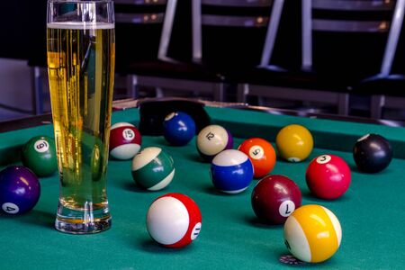 Colorful billiard balls sitting on pool table with glass of beerの写真素材
