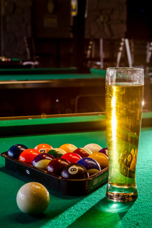 Colorful billiard balls in triangle rack with cue ball sitting on pool table with glass of beer