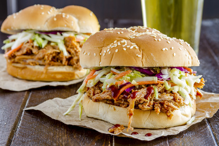 Two pulled pork barbeque sandwiches with coleslaw sitting on wooden table with glass of beerの写真素材