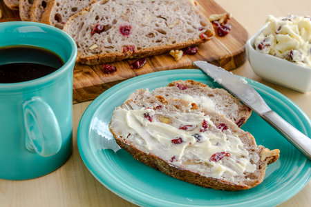 Slices of walnut cranberry bread with butter sitting on blue plate with cup of coffee