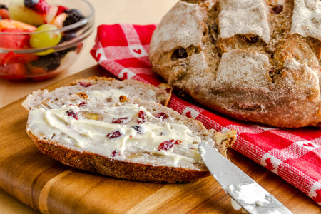 Whole loaf of walnut cranberry bread sitting on red heart napkin on wooden cutting board with slices...