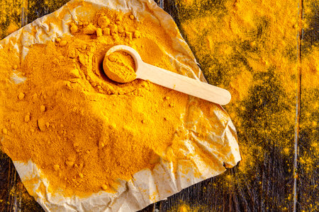Pile of organic turmeric (curcuma) powder sitting on brown paper with measuring spoon on wooden...