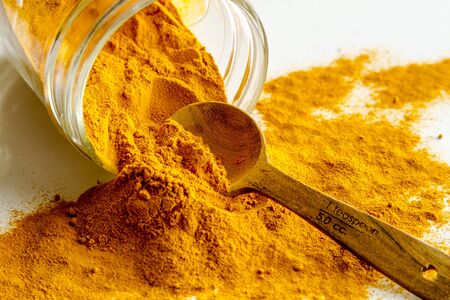 Organic turmeric (curcuma) powder in glass jar with measuring spoon on white backgroundの写真素材