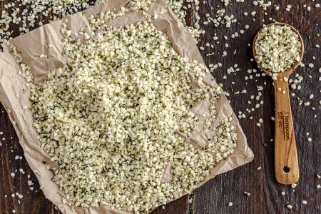 Pile of organic hemp seeds sitting on brown paper with measuring spoon on wooden tableの写真素材