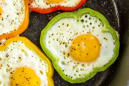 Close up of large cast iron skillet with fried eggs in green, yellow, red and orange bell peppersの写真素材