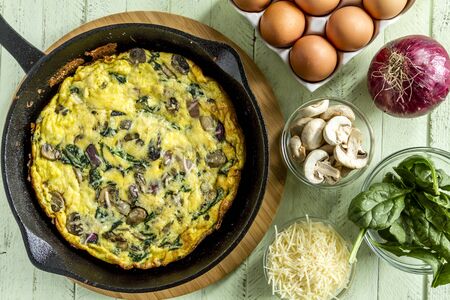 Spinach mushroom frittata sitting on wooden cutting board surrounded by raw ingredientsの写真素材