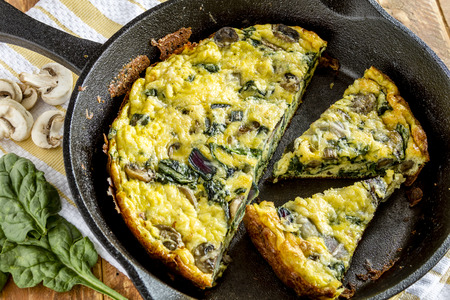 Close up of spinach mushroom frittata sitting on yellow striped kitchen towel with raw ingredientsの写真素材