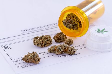 Medical marijuana buds spilling out of prescription bottle with lid onto blank medical prescription padの写真素材