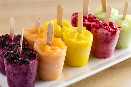 Assorted flavors of homemade fresh pureed frozen fruit popsicles sitting on white plate in a rowの写真素材