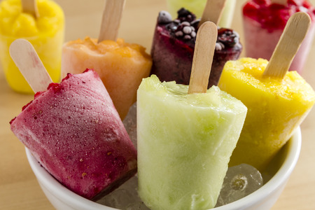 Close up of assorted flavors of homemade fresh pureed frozen fruit popsicles in white bowl with iceの写真素材