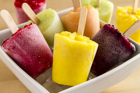 Close up of assorted flavors of homemade fresh pureed frozen fruit popsicles in white bowl with iceの写真素材