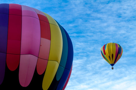Brightly colored hot air balloon against blue morning sky on the ground before take off and balloon in the airの写真素材