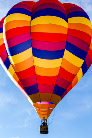 Brightly colored hot air balloon against blue morning sky just after take offの写真素材