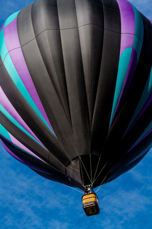 Brightly colored hot air balloon against blue morning sky just after take offの写真素材