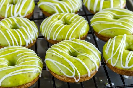 Homemade baked caramel apple donuts with green apple glaze sitting on wire baking rack after apple cider drizzle was appliedの写真素材