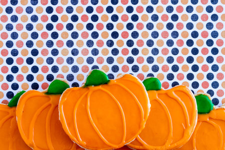 Homemade frosted pumpkin sugar cookies stacked on grunge polka dot background