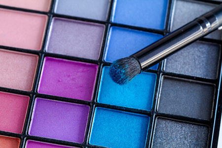 Cosmetic brush with bright blue eye shadow dust sitting on top of palette of blues and purples eye...