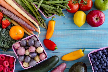 Variety of fresh raw organic fruits and vegetables in light pink containers sitting on bright blue wooden backgroundの写真素材