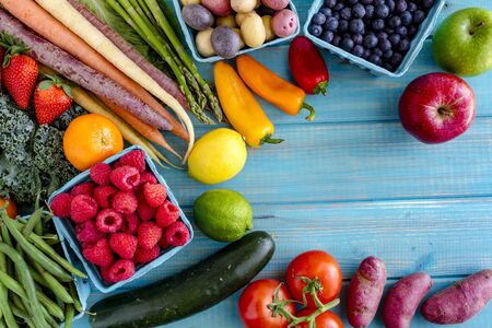 Variety of fresh raw organic fruits and vegetables in light blue containers sitting on bright blue wooden backgroundの写真素材