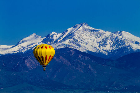 Bright yellow hot air balloon aloft in early morning blue sky over snow covered mountains in the distanceの写真素材