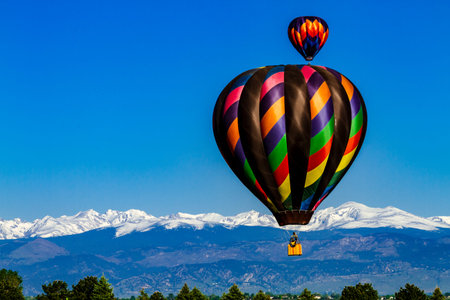 Brightly colored hot air balloons aloft in early morning blue sky over snow covered mountains in the...