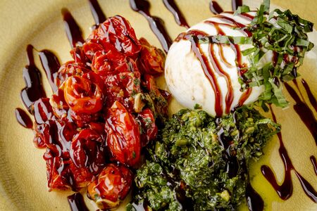 Close up of appetizer plate of burrata cheese with roasted roma tomatoes, nutless pesto and drizzled with aged balsamic vinegar shot from aboveの写真素材