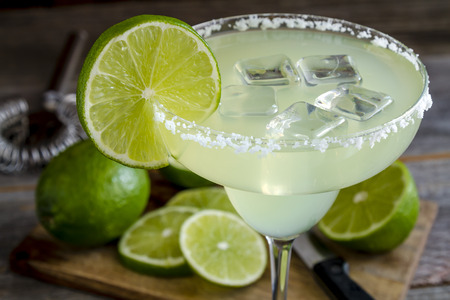Close up of classic lime margarita cocktail with sliced and whole limes sitting on wooden cutting boardの写真素材