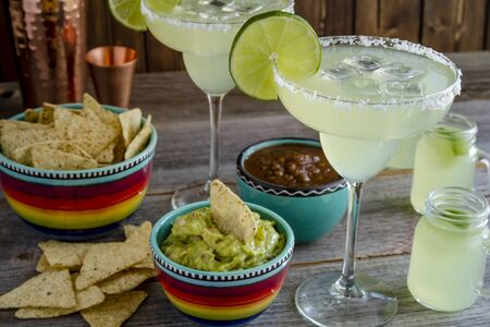 Table filled with glasses filled with classic lime margarita cocktails, tortilla chips, salsa and guacamoleの写真素材